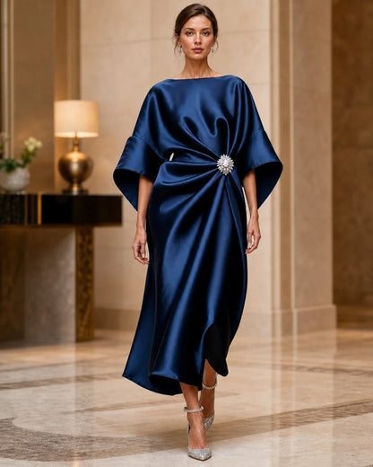 Women's navy satin midi evening dress with draped waist and wide batwing sleeves in an elegant interior.