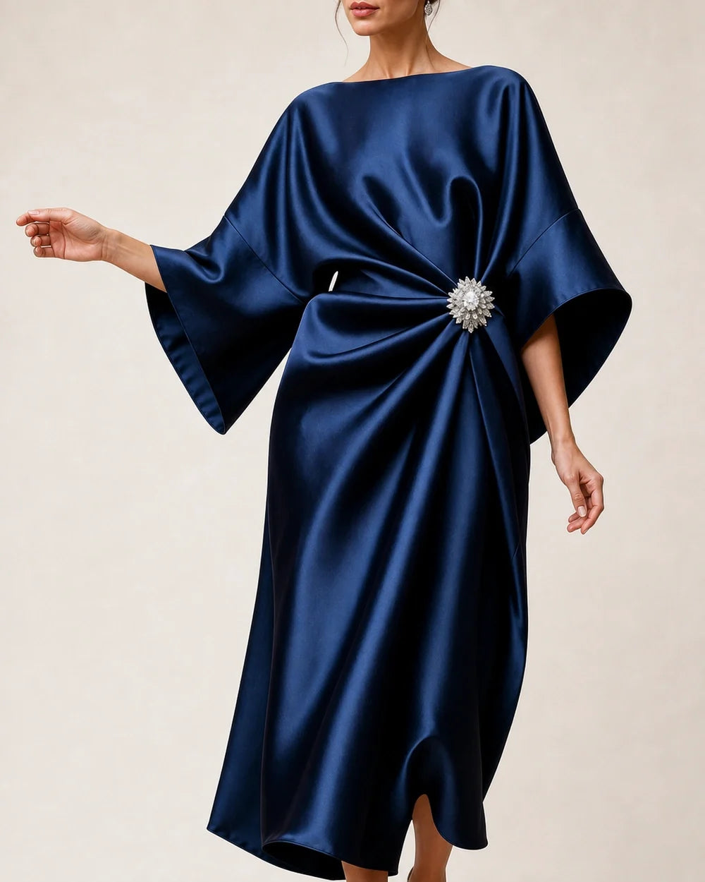 Close view of navy satin midi dress wide batwing sleeve, crystal flower brooch and gathered waist drape.